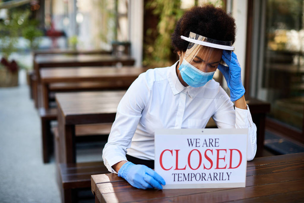 Black waitress holding closed sign and feeling worried about going out of business due to coronavirus pandemic.  - Photo, image