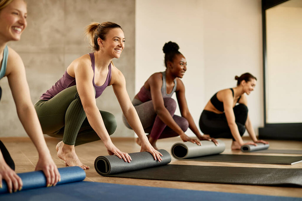 Щасливі спортивні жінки розкладають свої тренувальні килимки, готуючись до спортивних тренувань у спортзалі. Фокус на жінці в рожевій сорочці
. - Фото, зображення