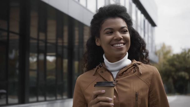 happy young african american woman holding coffee to go on street - Фото, изображение