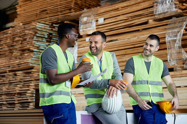 Happy workers having fun while talking with their manager on coffee break at lumber distribution warehouse. - Zdjęcie, obraz