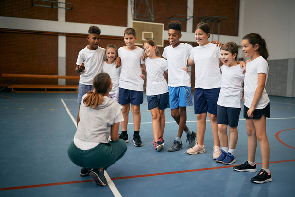 Group of happy elementary students with physical education teacher during a class at school gym.  - Foto, afbeelding