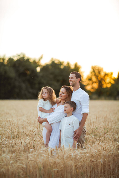 Прекрасная молодая семья на закате на пшеничном поле. Счастливые родители с двумя детьми, мальчик и девочка, в легкой одежде. Саммер. Любовь. - Фото, изображение