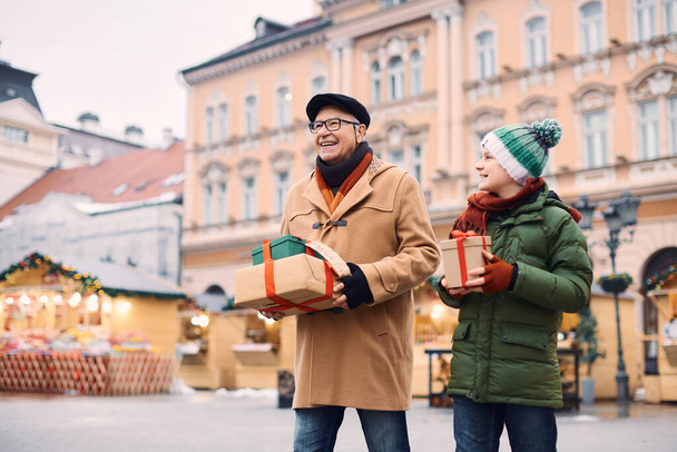 Happy little boy and his grandfather with gift boxes having fun during shopping at Christmas market.  - Photo, image