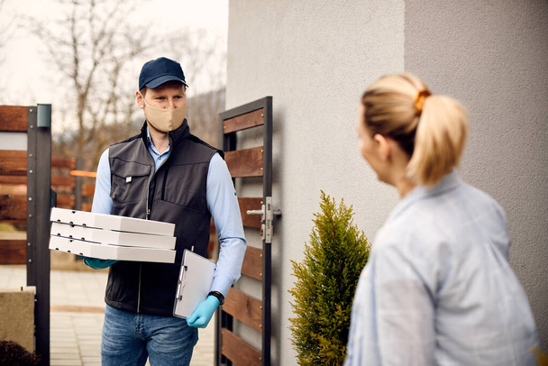 Food delivery man with protective face mask carrying pizza boxes while making home delivery to his customer. - Foto, immagini