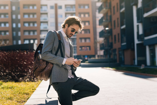 Молодий бізнесмен використовує мобільний телефон і вводить повідомлення в місті
.  - Фото, зображення