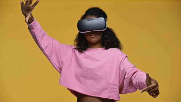 curly african american woman in pink sweatshirt and vr headset gesturing isolated on yellow  - Photo, image