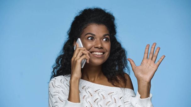 joyful african american woman in white knitted sweater talking on smartphone isolated on blue - Foto, immagini