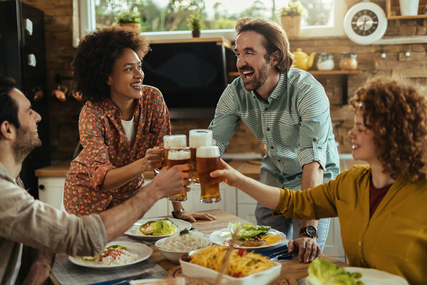 Group of young happy adult having lunch together and toasting with beer at dining table.  - Фото, изображение