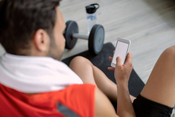 Close-up of athletic man texting on smart phone in health club. Copy space. - Foto, afbeelding
