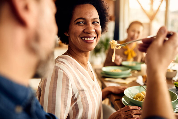 Щаслива чорна жінка дегустує макарони чоловіка, обідаючи з друзями в їдальні вдома
. - Фото, зображення