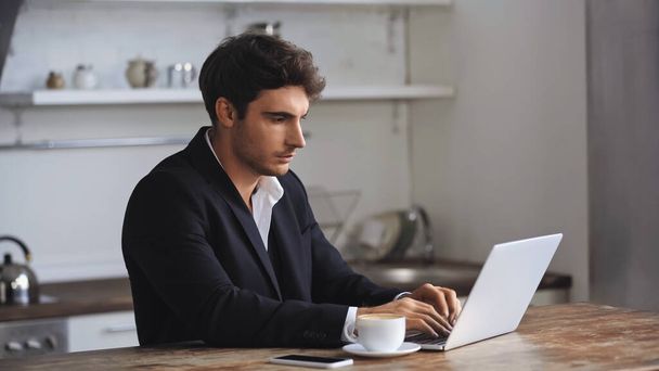 freelancer using laptop near smartphone and cup of coffee on desk - Foto, immagini