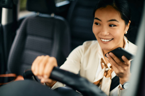 Щаслива азіатська бізнесменка користується смартфоном і посилає голосове повідомлення під час їзди автомобілем..  - Фото, зображення