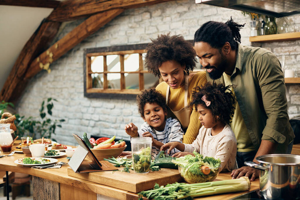 Happy African American family following recipe on touchpad while preparing healthy food in the kitchen. - Φωτογραφία, εικόνα