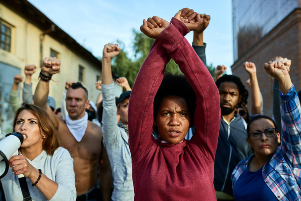 Black woman with clenched fists above her head protesting with group of people on the streets.  - Φωτογραφία, εικόνα