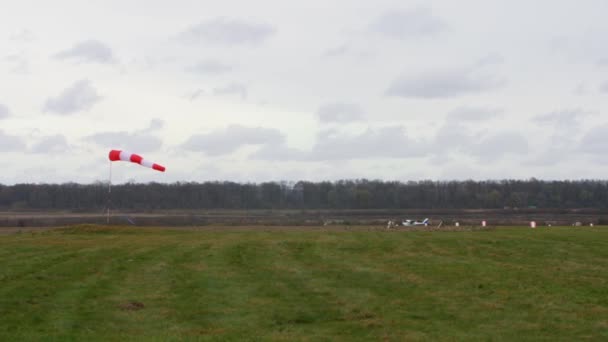 A white single-engine light plane takes off from the runway. Against the background of an autumn landscape and windsock. - Video, Çekim