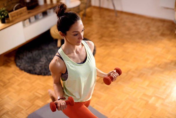 High angle view of athletic woman using dumbbells while doing lunges during home workout. - Photo, Image