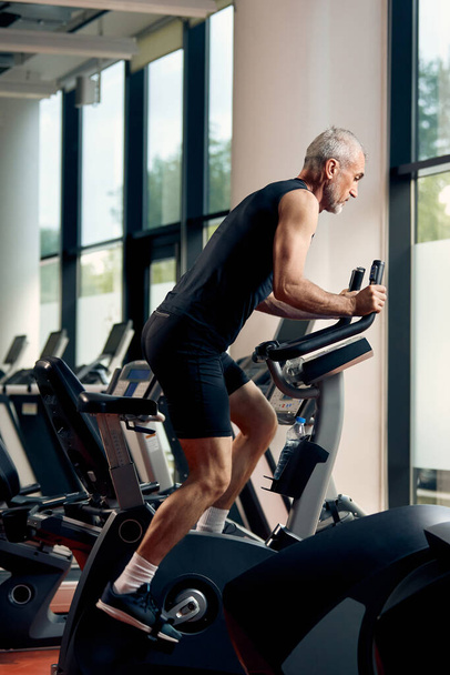 Mature athletic man during sports training on stationary bike in - Photo, Image