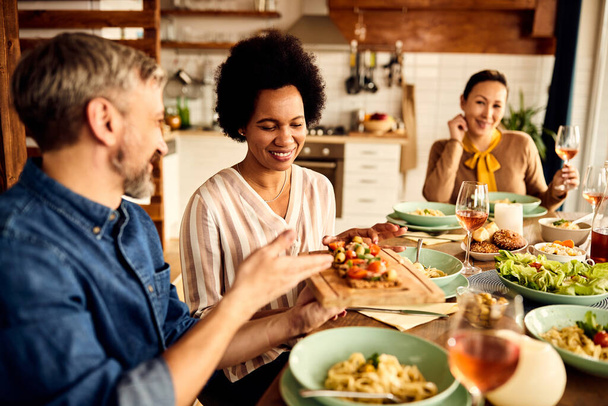 Smiling black woman tasting food while having dinner with friends at dining table. - Foto, Imagen