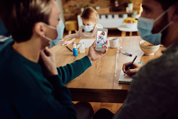 Close-up of a couple having video call with their family doctor from home due to coronavirus pandemic. Focus is on doctor on touchscreen.  - Foto, Imagen