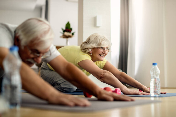 Mature couple doing relaxation exercises and stretching on the floor in the living room. Focus is on woman. - Photo, Image