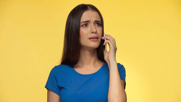 young brunette woman in blue t-shirt talking on smartphone isolated on yellow - Zdjęcie, obraz