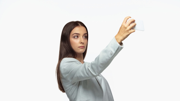 successful businesswoman in grey blazer taking selfie on smartphone isolated on white - Photo, image