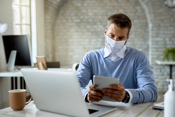 Businessman wearing protective face mask while using touchpad and working in the office.  - Foto, Imagen
