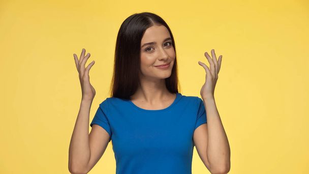 young and smiling woman in blue t-shirt gesturing isolated on yellow - Фото, зображення