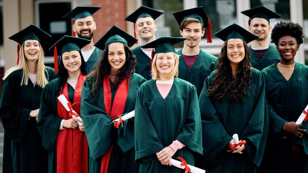 Велика група щасливих студентів університету в сукнях на день випуску дивиться на камеру
. - Фото, зображення