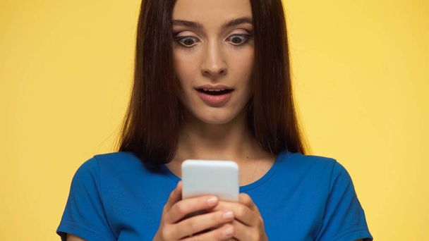 young and surprised woman chatting on mobile phone isolated on yellow - Foto, Imagen