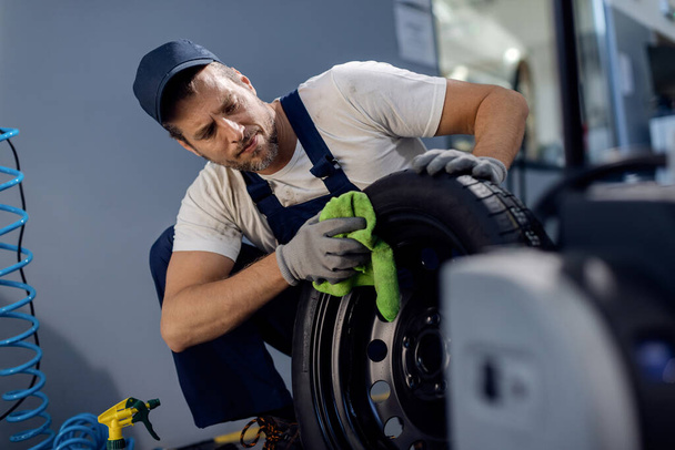 Středně dospělé auto mechanik čištění pneumatiky při práci v opravně. - Fotografie, Obrázek