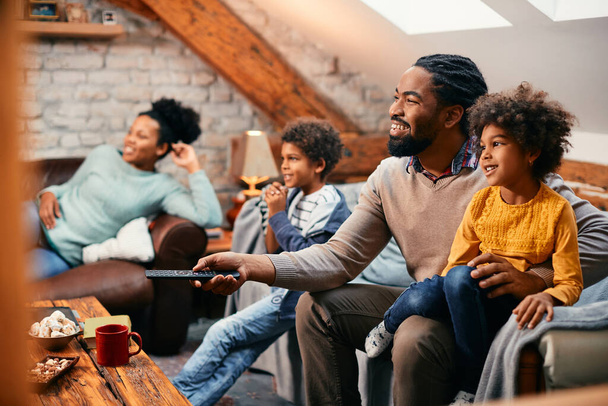 Счастливая афроамериканская семья смотрит телевизор, отдыхая вместе в гостиной. Сосредоточься на отце. - Фото, изображение