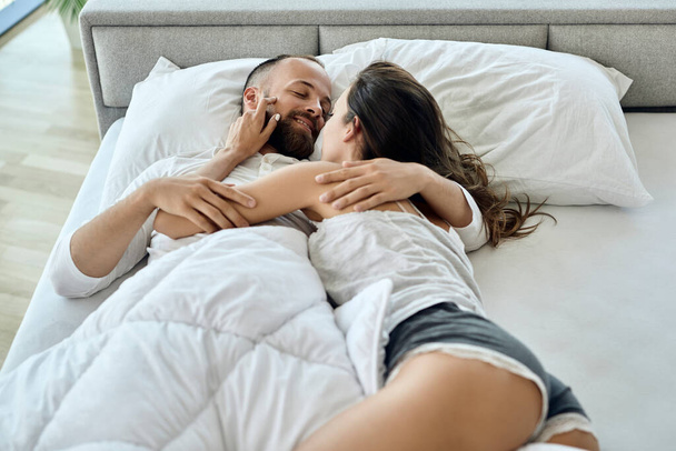 Young loving couple talking while lying down on bed in the morning.  - 写真・画像