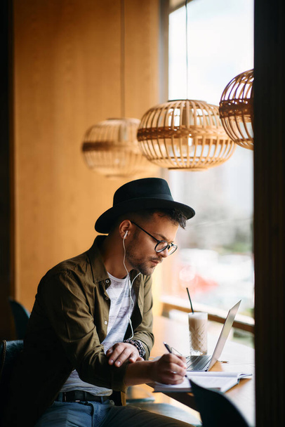 Молодой человек использует ноутбук и учится во время кофе-брейка в кафе.  - Фото, изображение