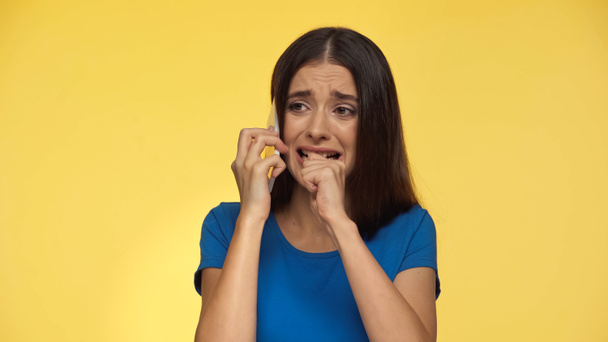 young brunette woman in blue t-shirt crying while talking on smartphone isolated on yellow - Photo, image