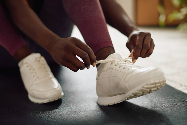 Close-up of African American athletic woman tying shoelaces while preparing for home workout.  - Foto, imagen