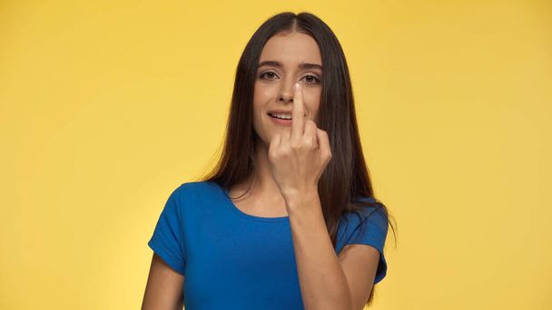 young and cheerful woman in blue t-shirt showing middle finger isolated on yellow - Photo, image