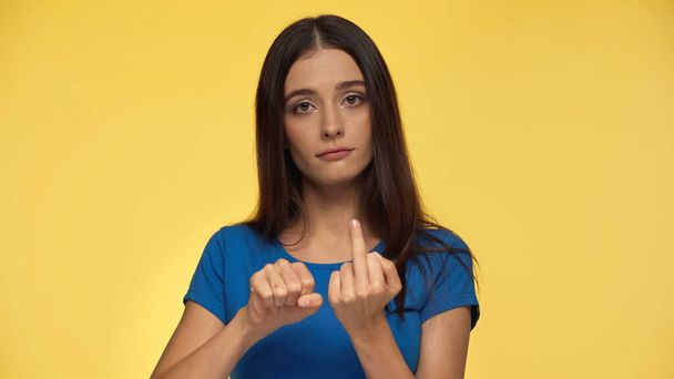 грубая молодая женщина в синей футболке показывает средний палец изолирован на желтый - Фото, изображение