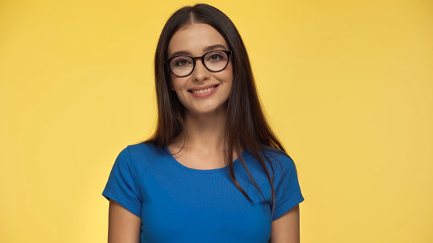 young and cheerful woman in blue t-shirt and eyeglasses looking at camera isolated on yellow - Valokuva, kuva