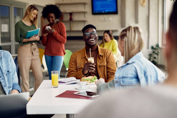 African American university student laughing while communicating with female colleague on lunch break in cafeteria.  - Foto, Imagen