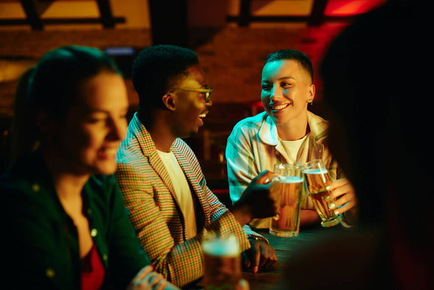 gelukkig zwart vrouw en haar vriend toasten met bier terwijl het op een date in een bar 's nachts.  - Foto, afbeelding