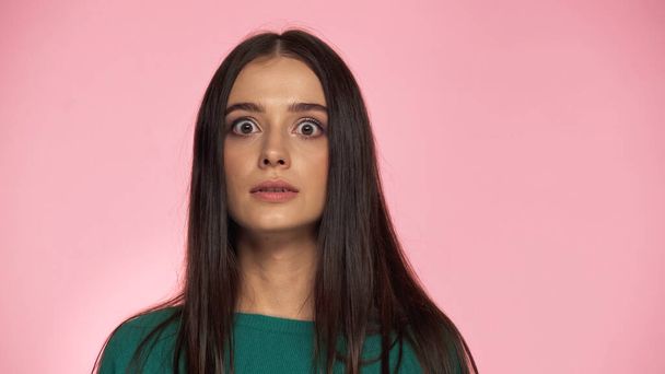 shocked brunette woman in green blouse looking at camera isolated on pink  - Foto, imagen