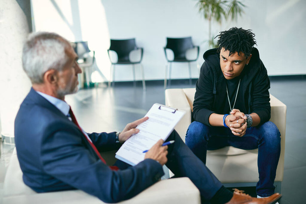 Black teenage boy with mental health issues communicating with his therapist during counselling session. - 写真・画像