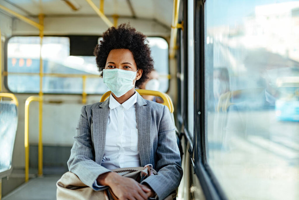 Toplu taşıma araçlarıyla seyahat ederken koruyucu maske takan Afrikalı Amerikalı iş kadını.  - Fotoğraf, Görsel