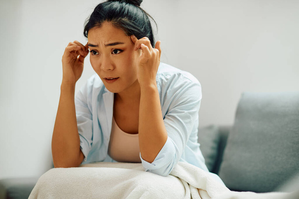 Genç endişeli Asyalı kadın evde oturup bir şeyler düşünürken baş ağrısı çekiyor.. - Fotoğraf, Görsel
