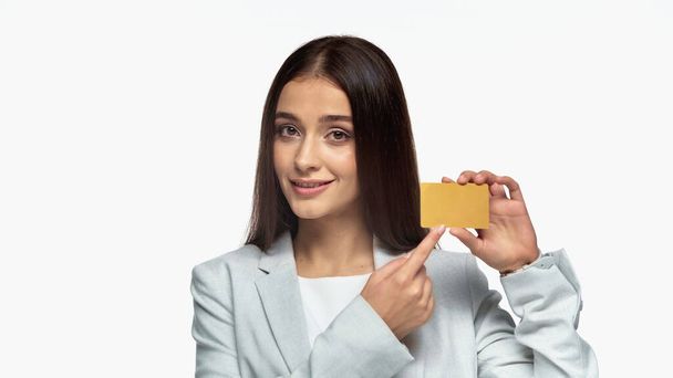 Gri ceketli başarılı bir iş kadını. Gülümsüyor ve beyaza izole edilmiş kredi kartını işaret ediyor. - Fotoğraf, Görsel