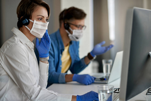 Агент колл-центра носит защитную маску во время использования компьютера и работы в офисе во время вирусной эпидемии.  - Фото, изображение