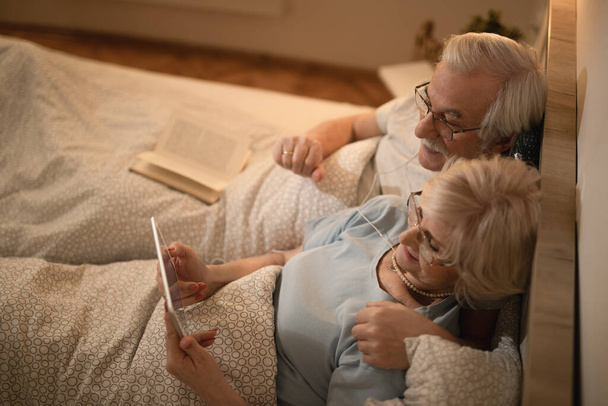 Magas látószögű kilátás idős pár segítségével digitális tabletta, miközben feküdt az ágyban éjszaka.  - Fotó, kép