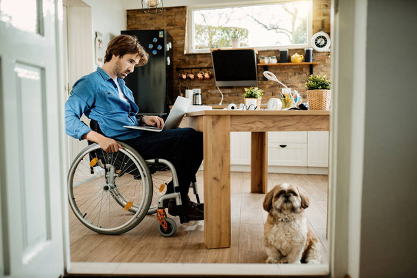 Fiatal fogyatékkal élő szabadúszó dolgozó dolgozik a számítógépen, miközben a kutyájával otthon.  - Fotó, kép