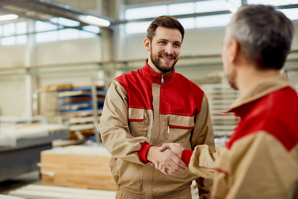 Happy carpenter handshaking with is colleague while greeting in a workshop.  - Foto, Imagem